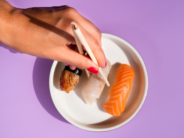 Free Photo woman taking a sushi from a white plate on blue background