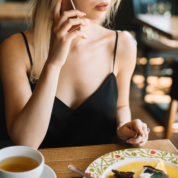 Woman talking on mobile phone while having breakfast in the caf���