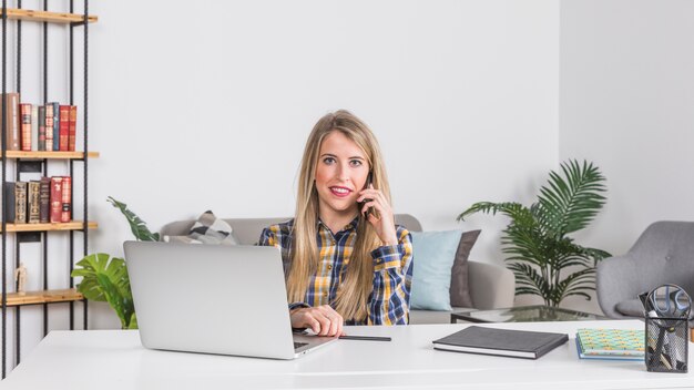 Woman talking on mobile phone at workplace at home 