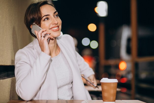 Woman talking on phone and drinking coffee outside in the street at night