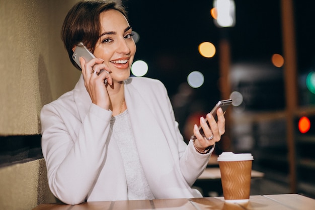 Woman talking on phone and drinking coffee outside in the street at night