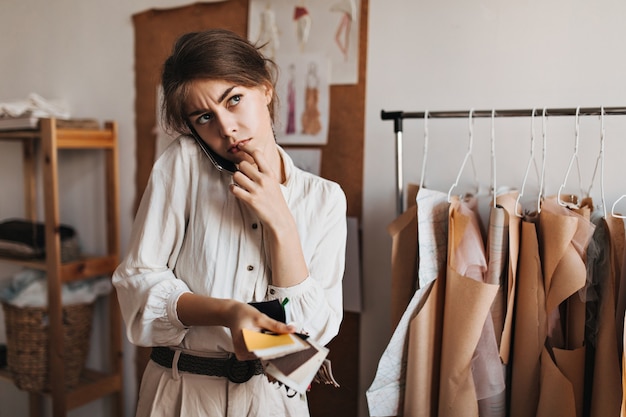 Free photo woman talking on phone, holding fabric samples and thoughtfully posing