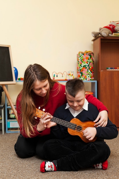 Woman teaching boy with down syndrome to play guitar