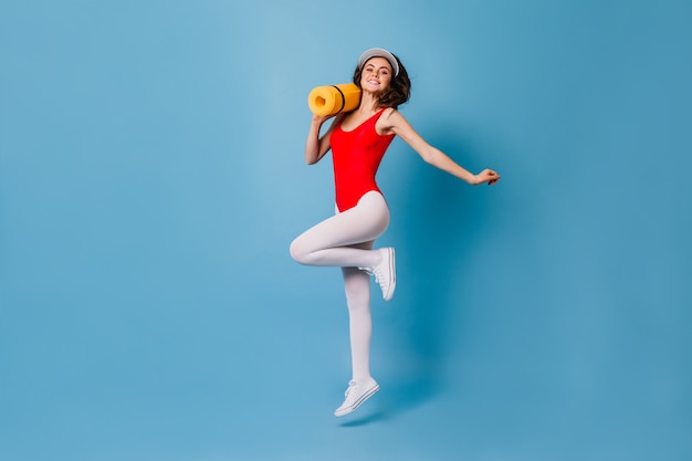 woman in tight spots suit happily jumps on blue wall