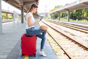 Free photo woman in a train station sitting on a luggage