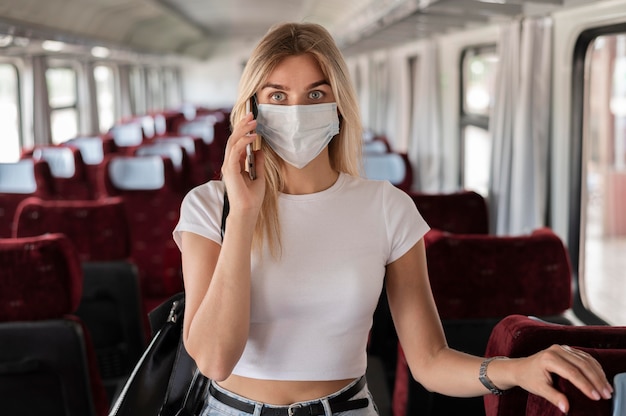 Woman traveling by train and talking on the phone while wearing medical mask