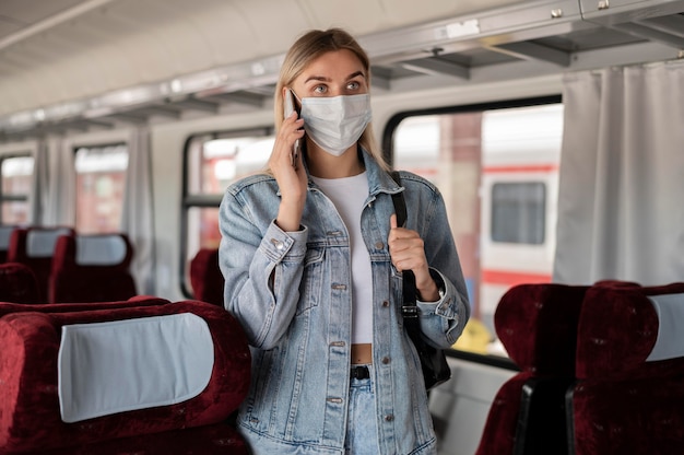 Free photo woman traveling by train and talking on the phone while wearing medical mask