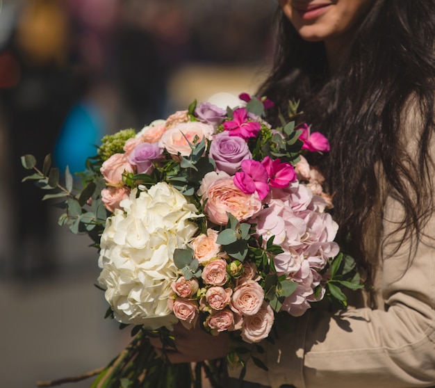 Woman in trench coat holding a mixed bouquet of winter flowers.