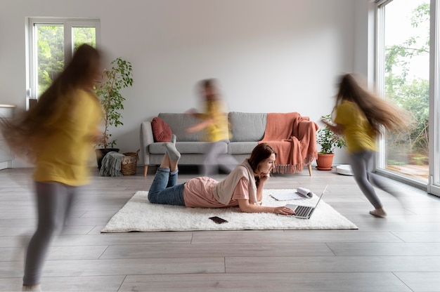 Free photo woman trying to work on laptop from home while her children are running around