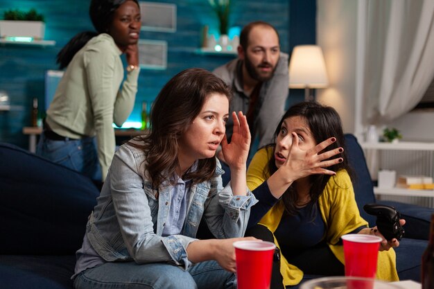 Woman upset after lose at online video games while having socializing with multi ethnic group of friends in home living room late at night, drinking beer.