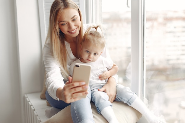 Woman uses the phone.  Mother in a white shirt is playing with her daughter. Family has fun on the weekends.