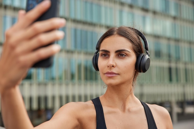 Free photo woman uses phone for online call or taking selfie on front camera during fitness workout has confident expression spends free time in urban place