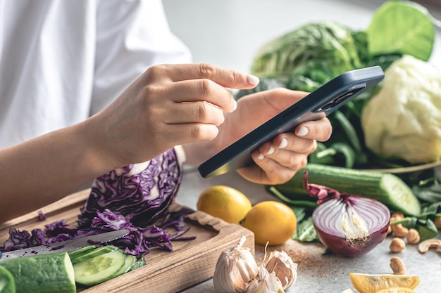 Free photo a woman uses a smartphone in the kitchen while preparing a vegetable salad