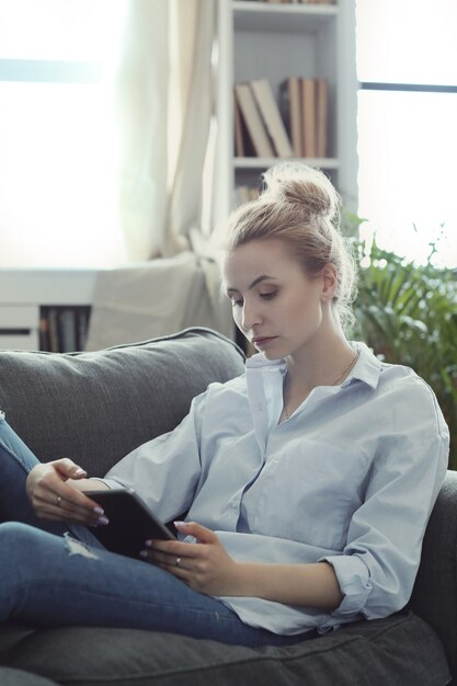 woman using digital tablet, lying on sofa