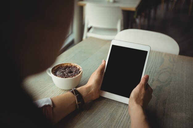 Woman using digital tablet while having cup of coffee