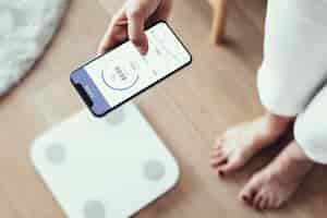 Free photo woman using health tracking on her phone by the weighing scale  innovative technology