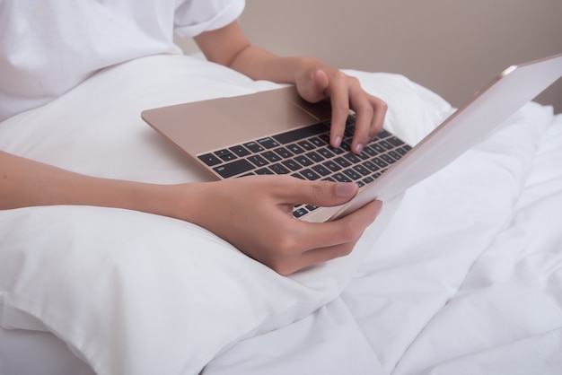 Woman using laptop smiling sitting on bed at home woke up in the morning