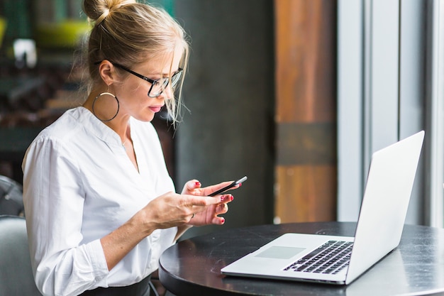 Free Photo woman using smartphone with laptop on desk