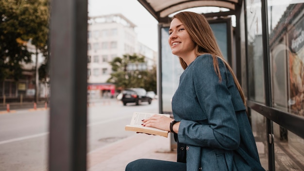 Woman waiting for the bus and holding a book