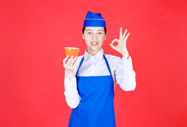 Woman waitress in uniform holding an orange bowl and showing ok gesture .