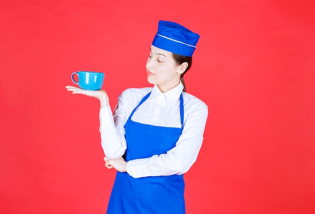 Free photo woman waitress in uniform standing and holding a bowl on red wall.