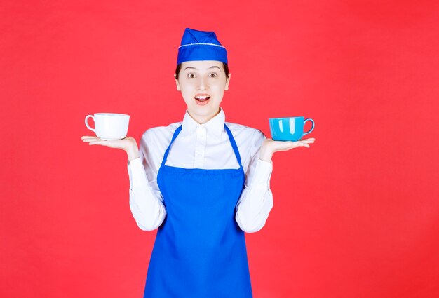 Woman waitress in uniform standing and holding colorful cups on red wall .