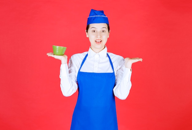 Woman waitress in uniform standing and holding a green bowl .