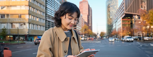 Free photo woman walking on street using digital tablet holding gadget in hands and looking away standing in