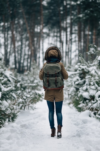 Free Photo woman in warm winter jacket with fur hood and big travel rucksack in snowy winter forest