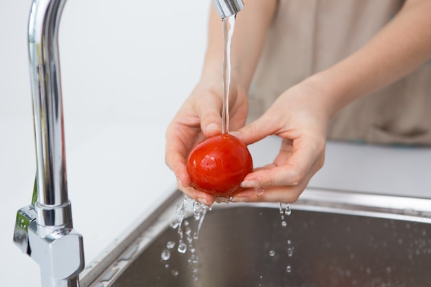 Free photo woman washing tomato with tap water