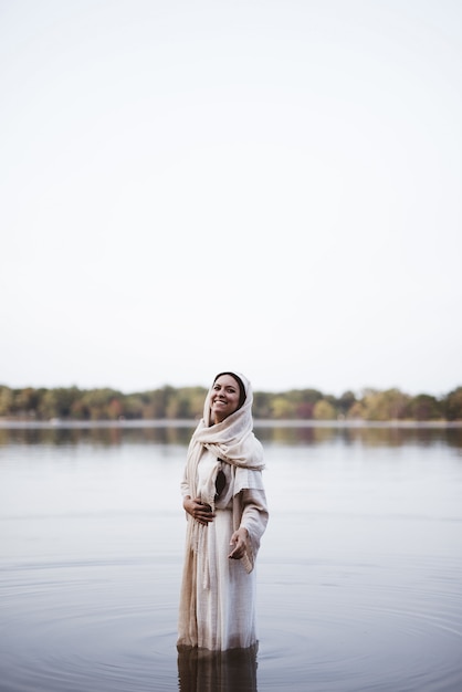 Woman wearing a biblical robe while standing in the water and smiling