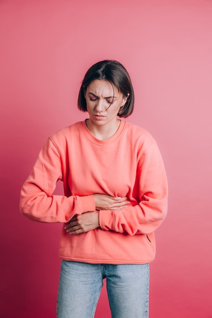 Free photo woman wearing casual sweater on background suffering stomach ache with painful grimace, feeling sudden period cramps, gynecology concept