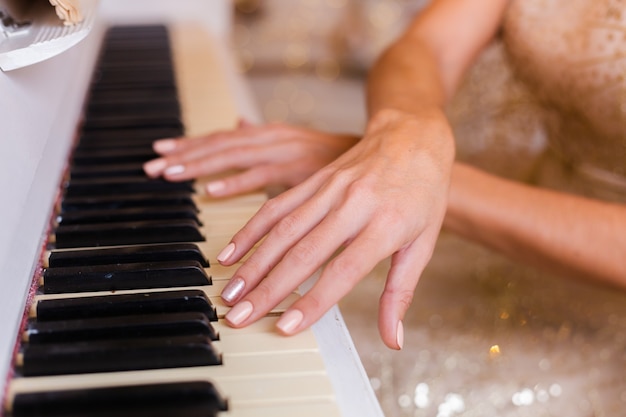 Free photo woman wearing evening shiny golden christmas dress playing piano at home.