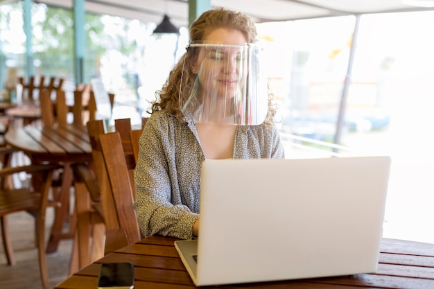 Woman wearing face protection while working on laptop