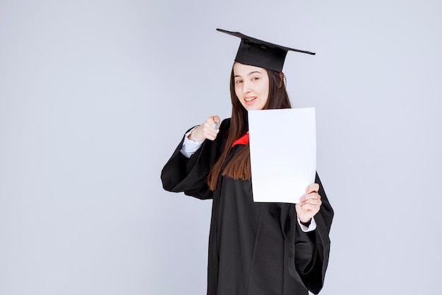 Woman wearing graduation cap holding pen and empty sheet. High quality photo