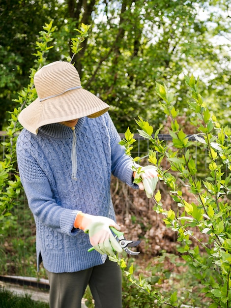 Free Photo woman wearing a hat while cutting leaves from her garden