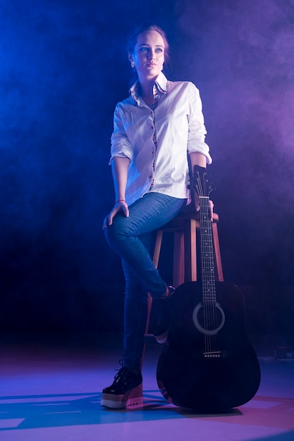 Woman wearing office shirt holding an acoustic guitar