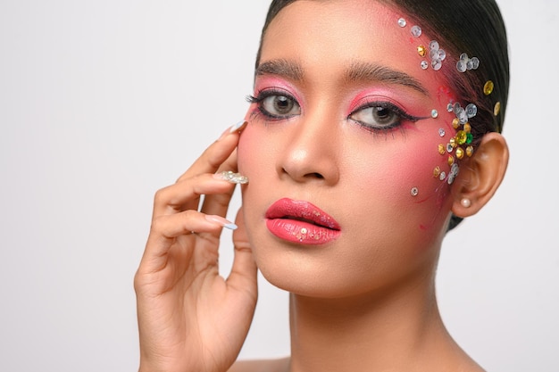 Woman wearing pink makeup and embellishments on her face isolated on white