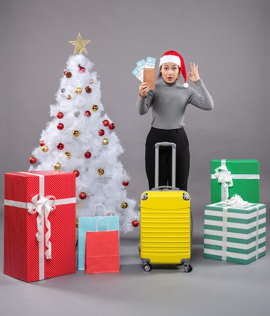 Free photo woman wearing santa claus hat with luggage next to christmas tree