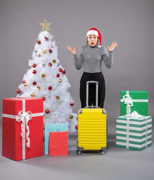 Free photo woman wearing santa claus hat with luggage next to christmas tree