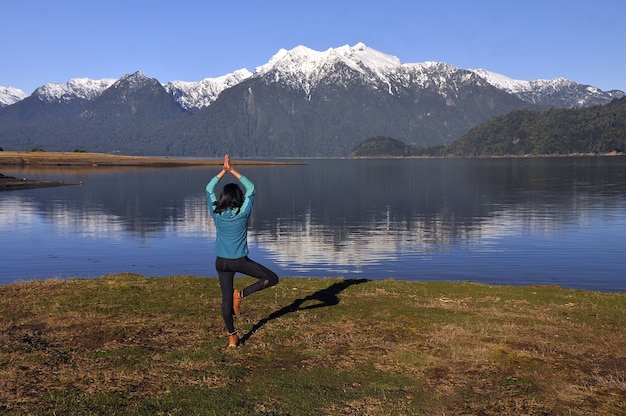 Woman wearing sportswear, holding a yoga pose in front of the calm lake and mountains