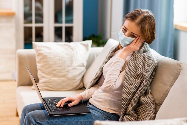 Woman wearing surgical face mask and sitting on couch