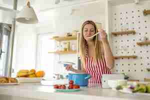 Free photo woman wearing a white apron with red lines and cooking something in the kitchen