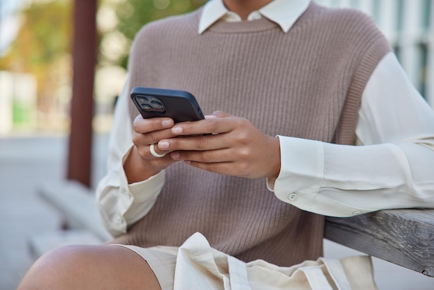 Free Photo woman wears neat clothes uses mobile phone sends text messages and mails chats onlie sits on wooden bench