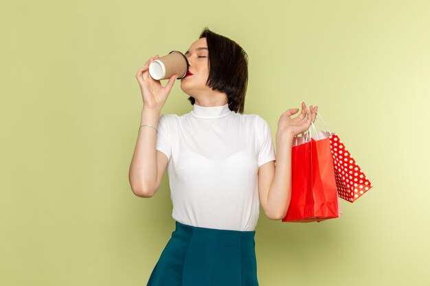 woman in white blouse and green skirt holding shopping packages and drinking coffee 