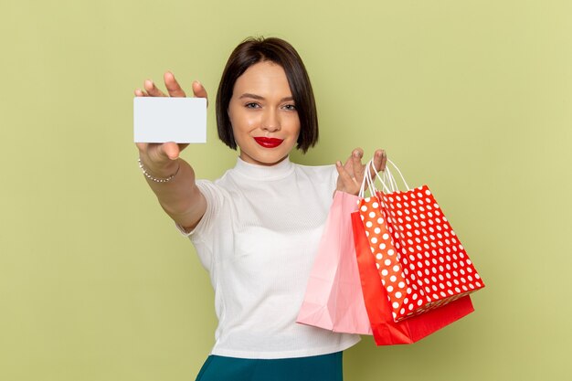 woman in white blouse and green skirt holding shopping packages and showing white card 