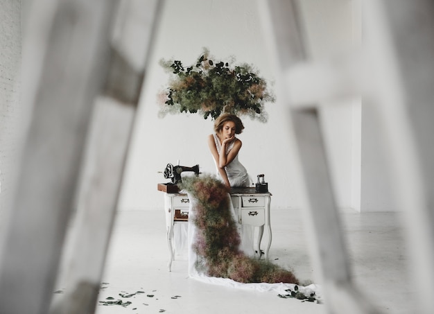 Free Photo woman in white clothes sits in a room with flowers and sewing machine