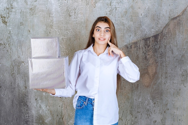 woman in white shirt holding silver gift boxes and looks confused