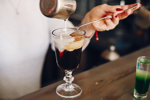 Woman in a white sweater pouring milk into coffee dessert