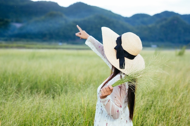 A woman who is holding a grass in her hands on a beautiful grass field with a mountain .